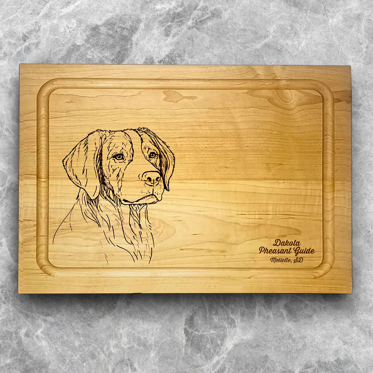 A high-quality, durable maple cutting board with juice groove featuring a laser-engraved Brittany Spaniel. A perfect addition for any kitchen, and a wonderful reminder of your love of hunting and sporting dogs. A Dakota Pheasant Guide souvenir.