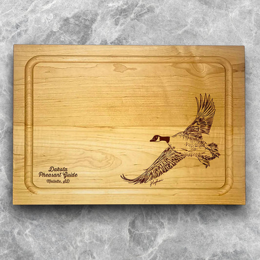 A high-quality, durable maple cutting board with juice groove featuring a laser-engraved Canada Goose in flight. A perfect addition for any kitchen, and a wonderful reminder of your love of hunting and game birds. A Dakota Pheasant Guide souvenir.