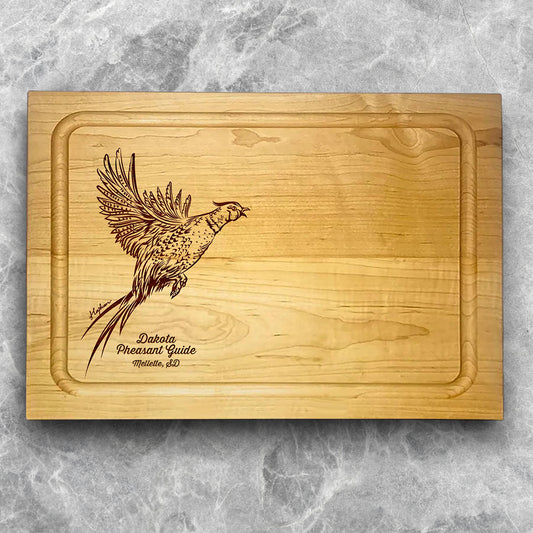 A high-quality, durable maple cutting board with juice groove featuring a laser-engraved Pheasant taking flight. A perfect addition for any kitchen, and a wonderful reminder of your love of hunting and game birds. A Dakota Pheasant Guide souvenir.