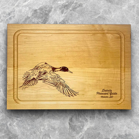 A high-quality, durable maple cutting board with juice groove featuring a laser-engraved Pintail Duck in flight. A perfect addition for any kitchen, and a wonderful reminder of your love of hunting and game birds. A Dakota Pheasant Guide souvenir.