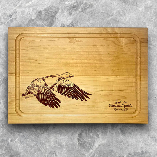 A high-quality, durable maple cutting board with juice groove featuring a laser-engraved Snow Goose in flight. A perfect addition for any kitchen, and a wonderful reminder of your love of hunting and game birds. A Dakota Pheasant Guide souvenir.