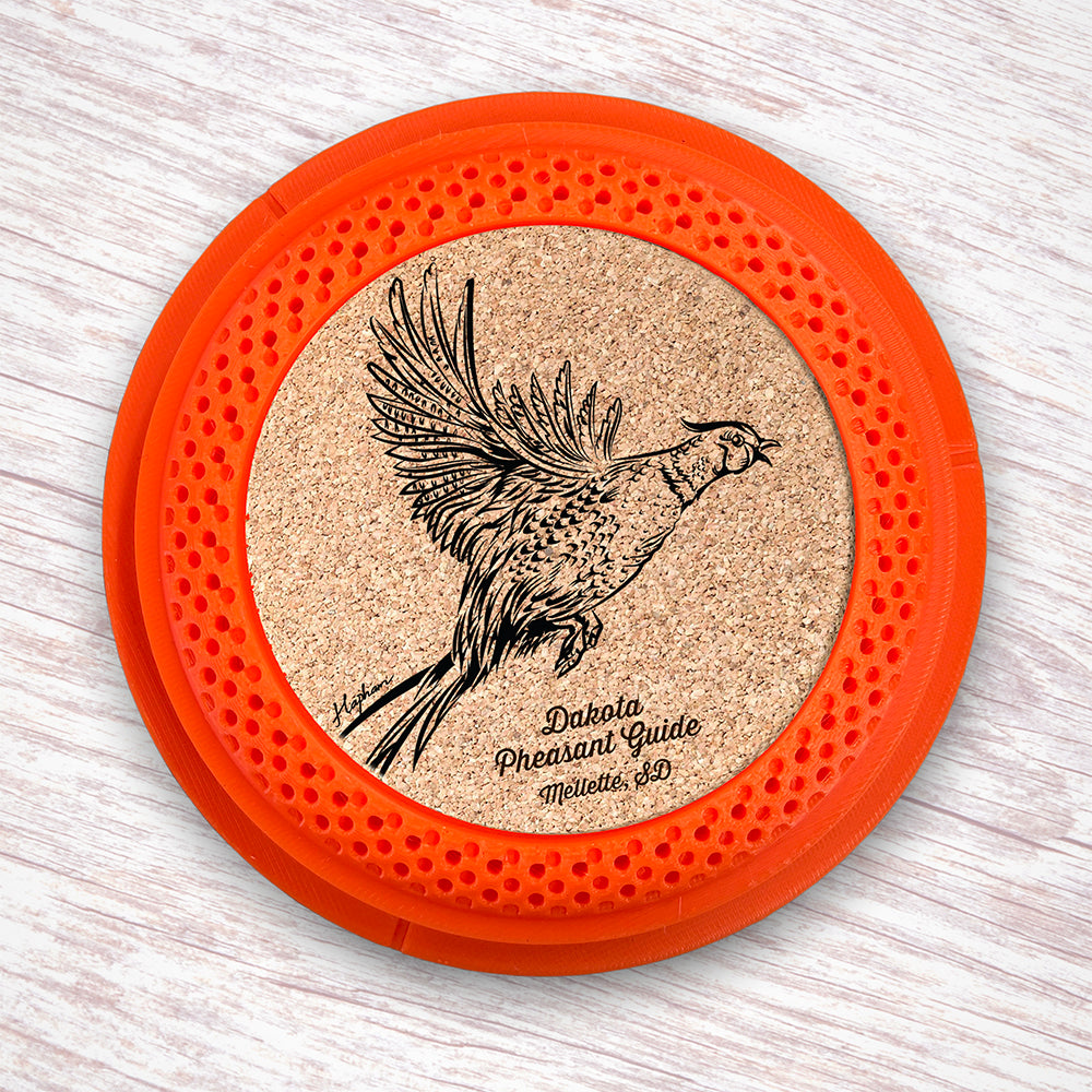 Clay Pigeon shaped coaster base with a laser-engraved cork insert featuring a Pheasant taking flight - this set of 4 coasters makes a unique gift for any trap shooter, gun enthusiast and bird dog lover! By Muggins Gifts for the Dakota Pheasant Guide Souvenir shop.