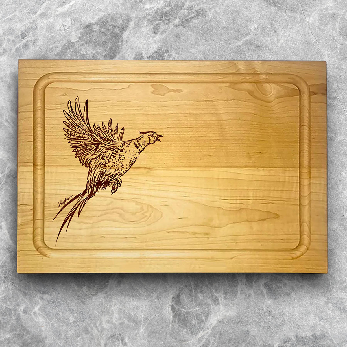 A high-quality, durable maple cutting board with juice groove featuring a laser-engraved Pheasant taking flight. A perfect addition for any kitchen, and a wonderful reminder of your love of hunting and game birds. A Dakota Pheasant Guide souvenir.